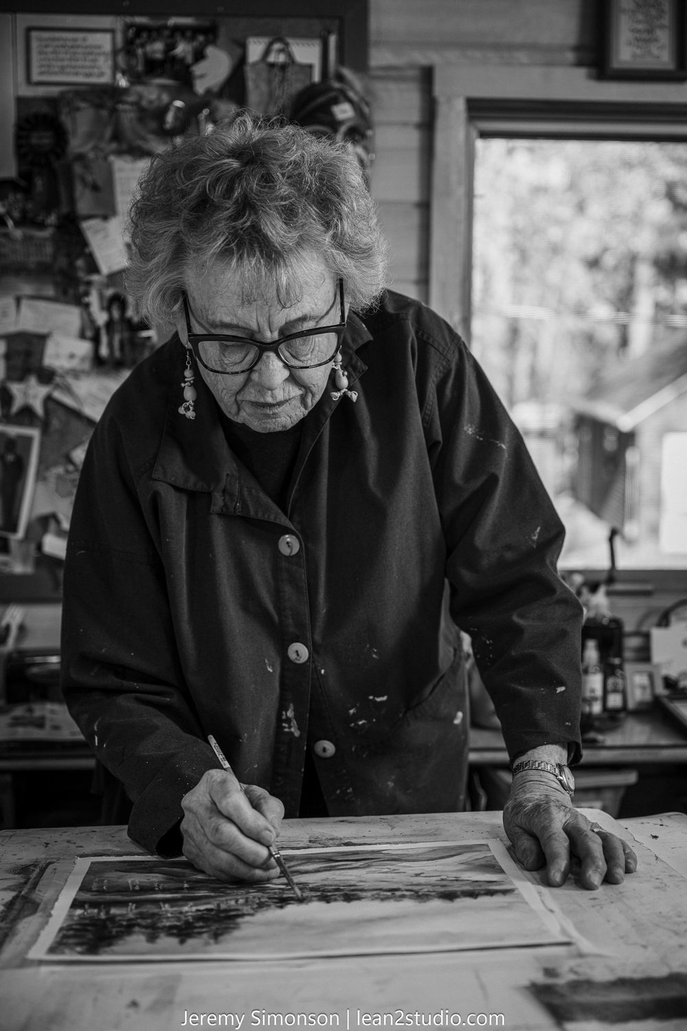 A series of black and white photographs showing someone in glasses working intently on detailed paperwork at a desk.