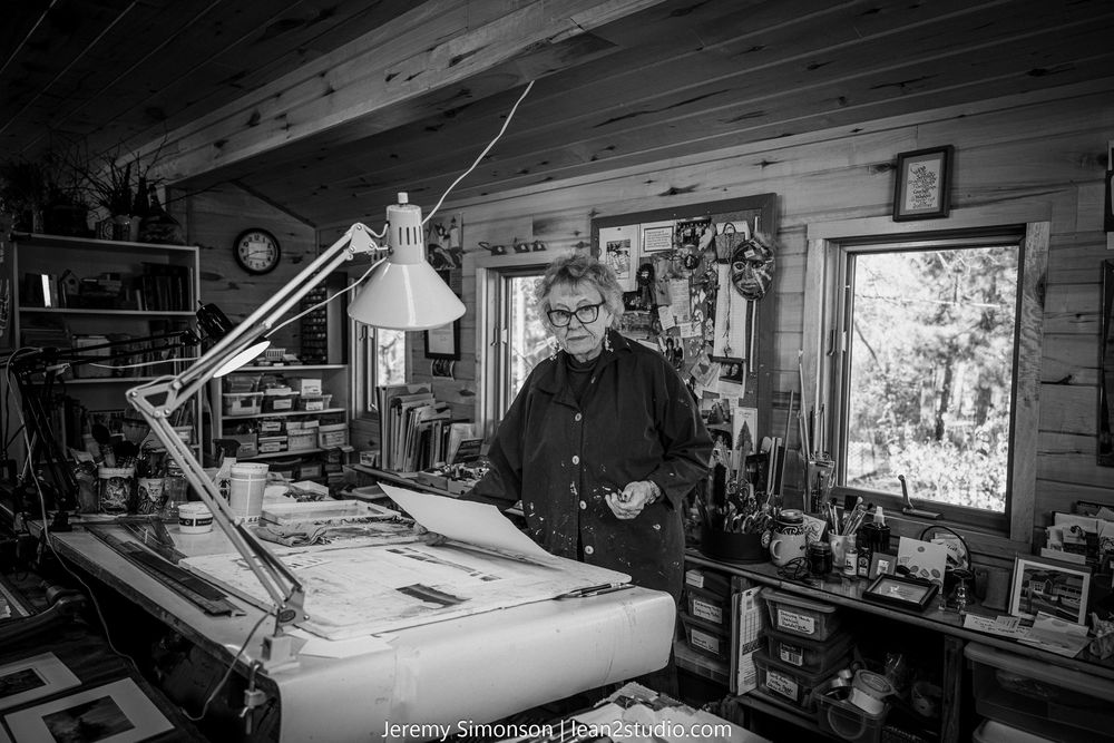 A panoramic view of a cluttered workshop interior with tools, equipment and storage shelves in black and white.