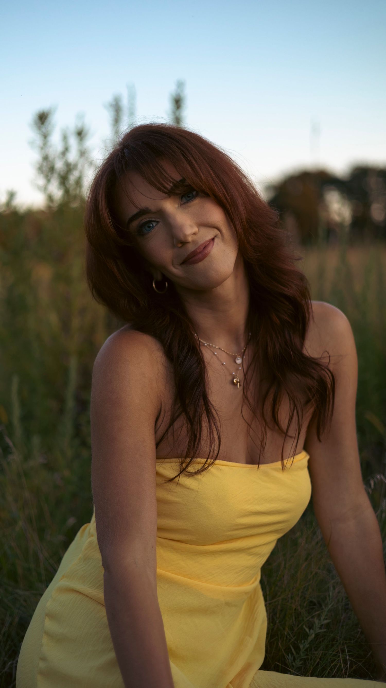 A person in a yellow sundress sits in a grassy field at sunset with a warm summer evening glow.