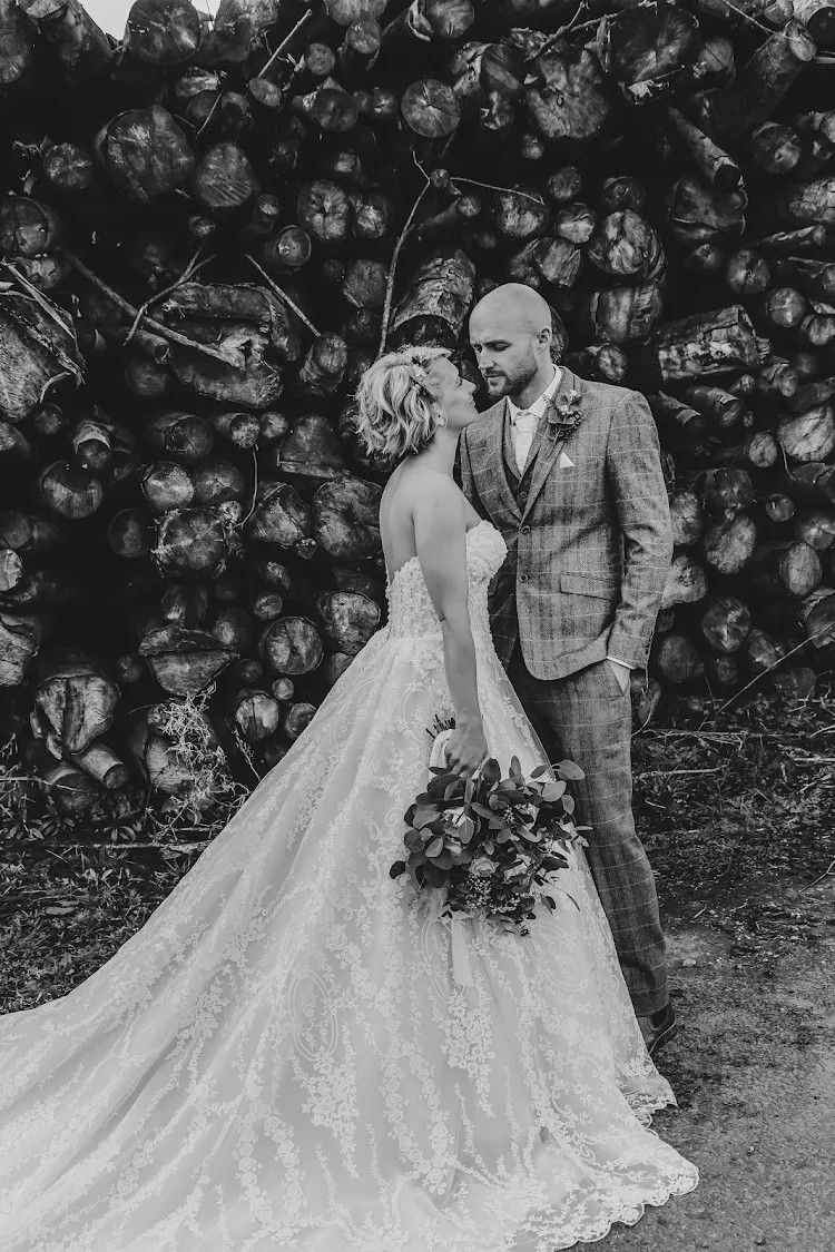 Black and white wedding photos showing a couple in formal attire posing together with a woodpile backdrop.
