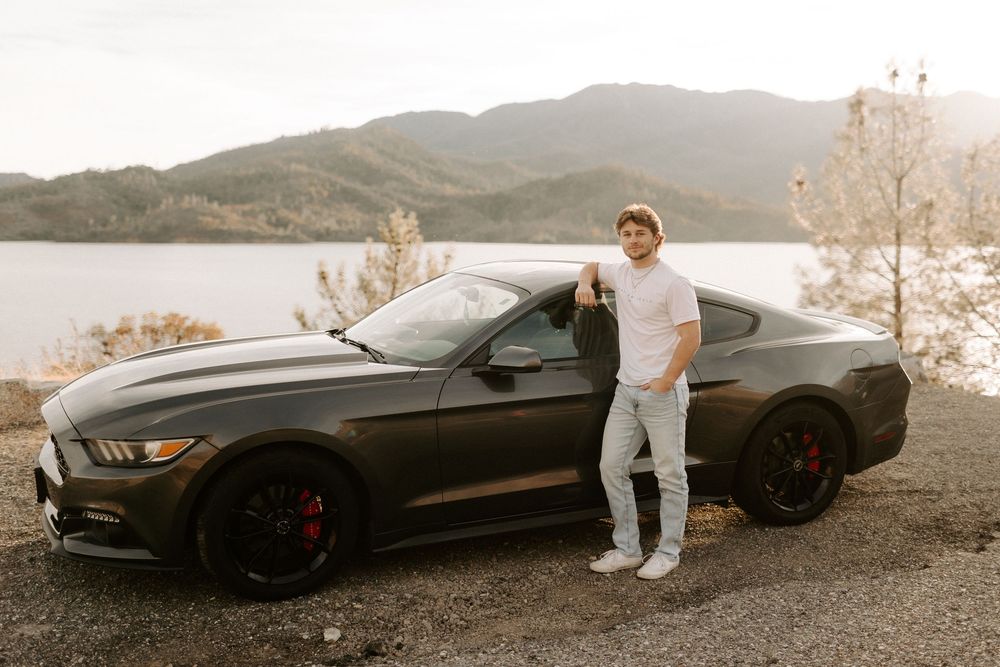 A black sports car parked on a mountain road during sunset with scenic views in the background.