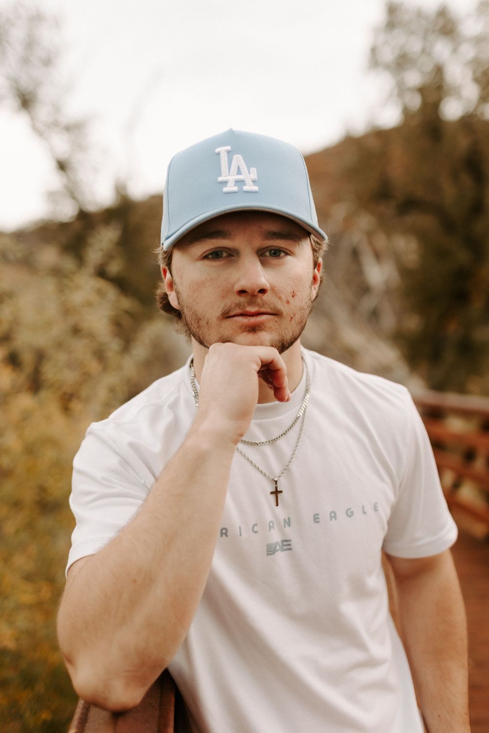 Person in white t-shirt and LA Dodgers baseball cap posing outdoors in warm lighting.