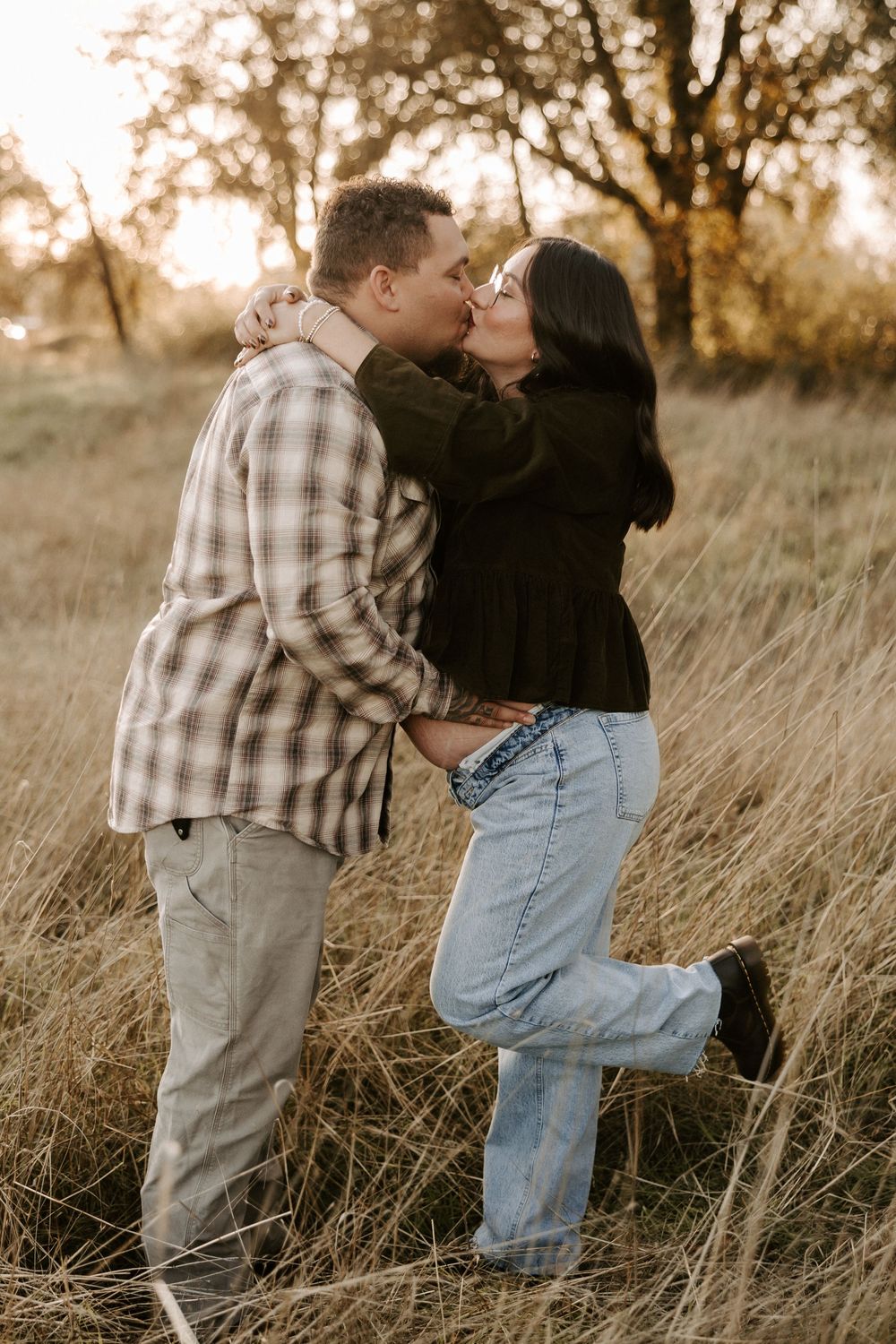 A couple shares an intimate moment in a golden field of tall grass at sunset.