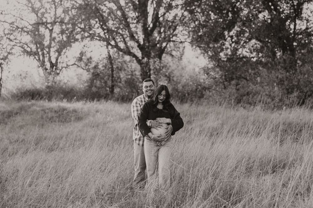 Black and white photo of someone standing in a tall grass field with trees in the background.