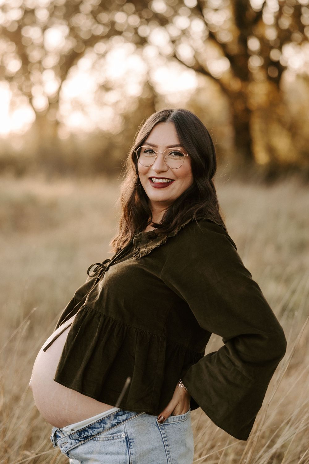 A person in a black sweater and jeans sits in tall grass during golden hour with warm autumn lighting.