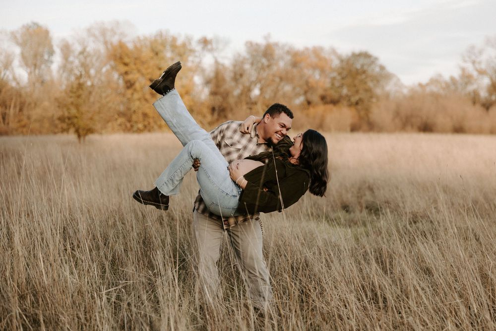 A couple shares a playful moment in a golden autumn field during sunset.