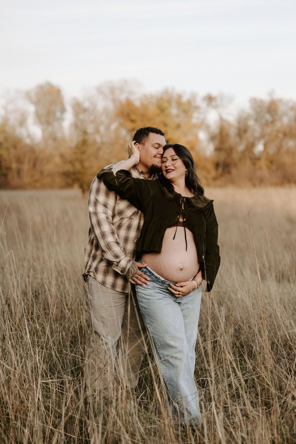 Intimate couple embraces in a golden autumn field during sunset maternity photoshoot.