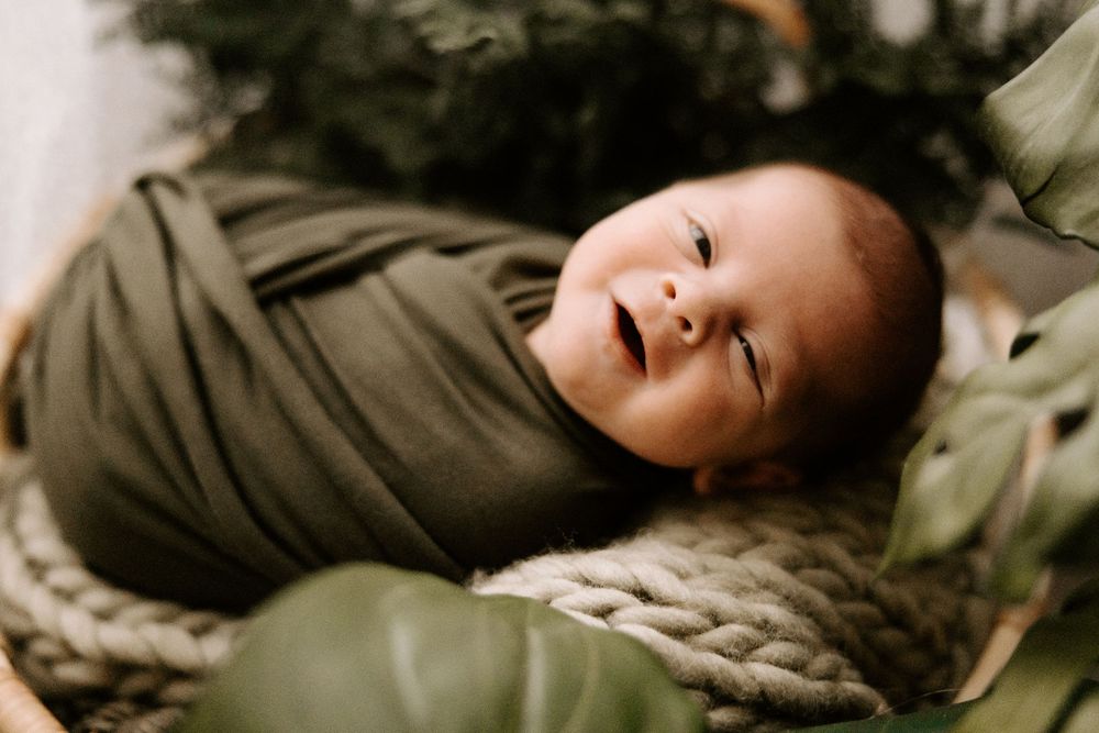 Overhead view of a newborn baby swaddled in olive green fabric lying on a textured surface.