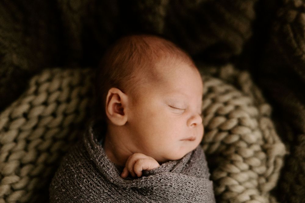 A sleeping newborn baby wrapped in a cozy brown knit blanket during a professional photography session.