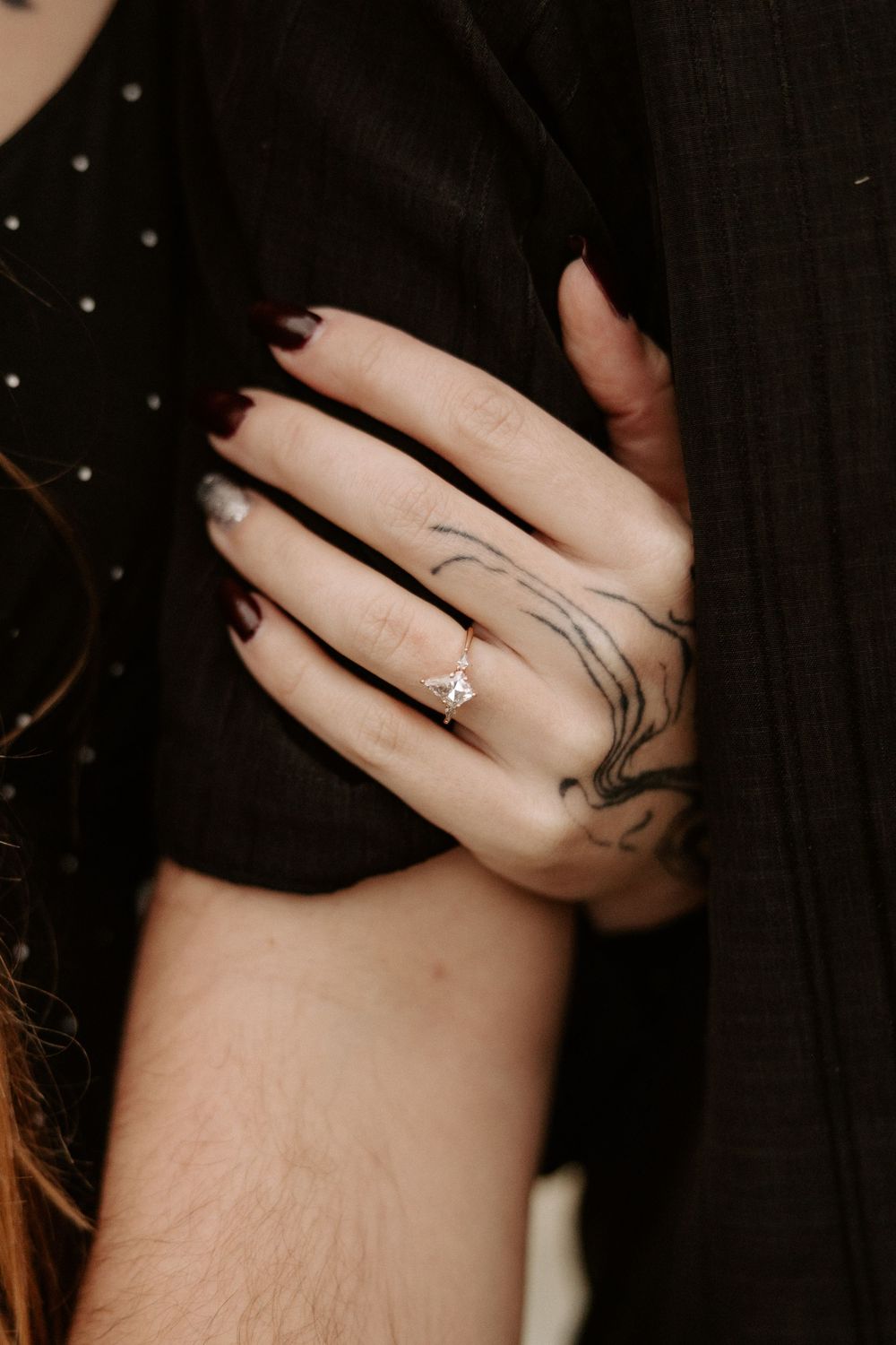 Close-up shot of a hand with delicate tattoos wearing an elegant diamond engagement ring.