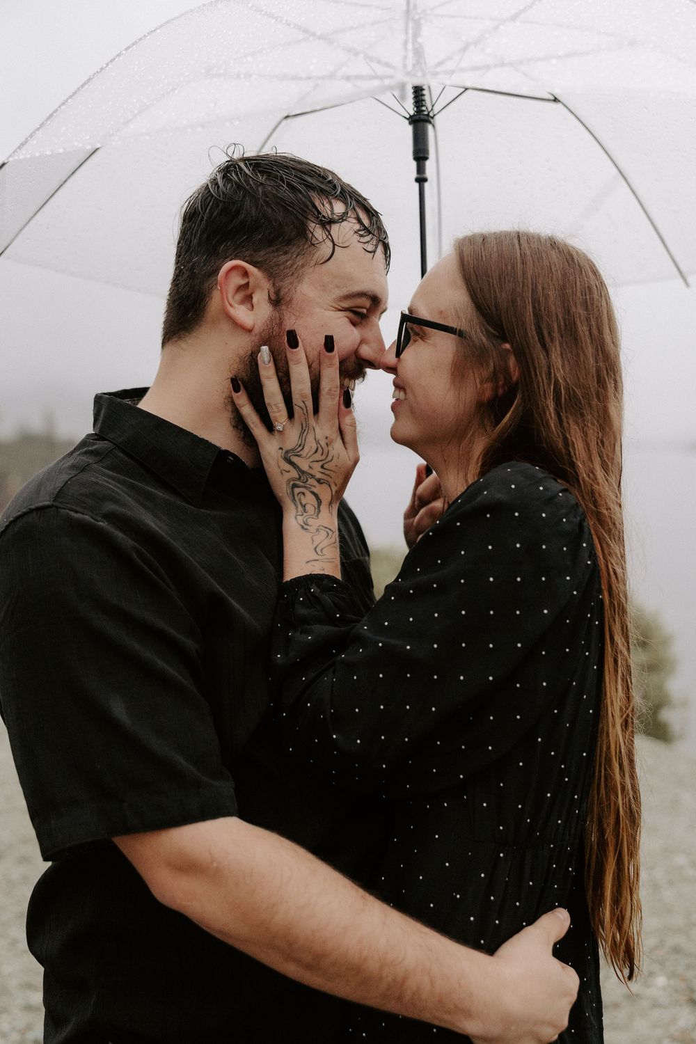 Romantic couple sharing intimate moments under a white umbrella in moody weather.