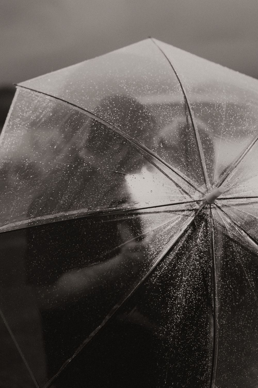 Raindrops sparkle and splash against a clear umbrella in black and white, creating a mesmerizing pattern.