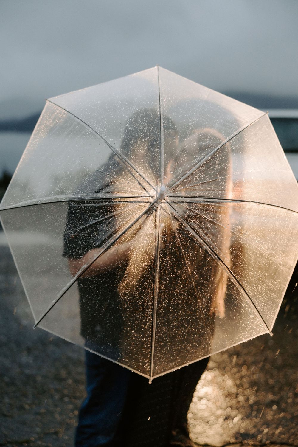 A transparent umbrella glows with golden sunlight while water droplets create a magical effect against the sky.