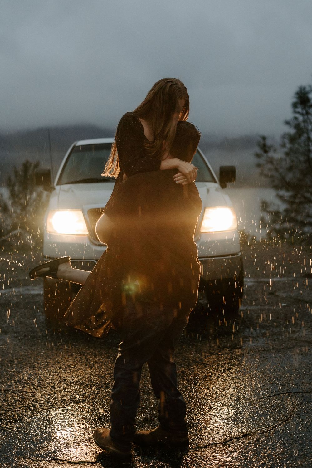 Silhouette of a person in front of car headlights on a rainy evening with water splashing around them.