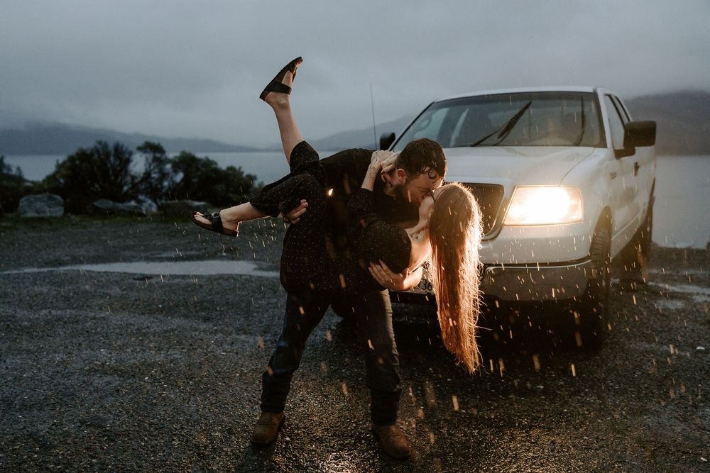 A dramatic silhouette of people dancing in front of a car's headlights on a rainy evening.