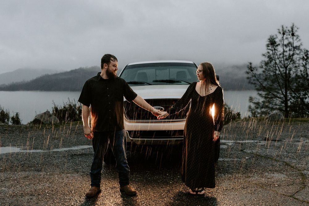 Couple sitting on the back of a pickup truck overlooking a misty mountain landscape at sunset.