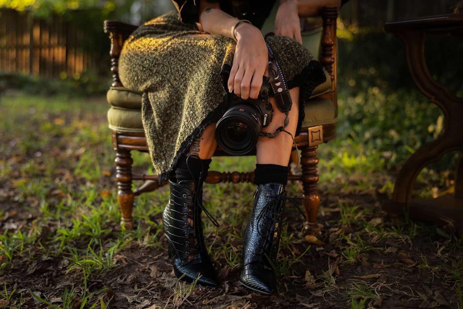 a woman, sitting in a chair, holding a camera from the waist down.