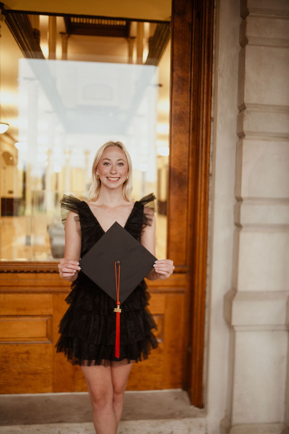 Graduation photo of a client posing with her grad cap, with the iconic Mizzou Columns reflected in the window behind her.