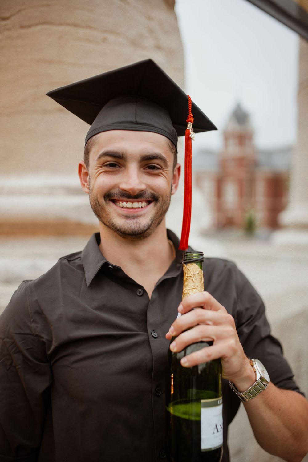 Graduation photo of a client wearing a cap at the Mizzou Columns, laughing and celebrating with champagne.