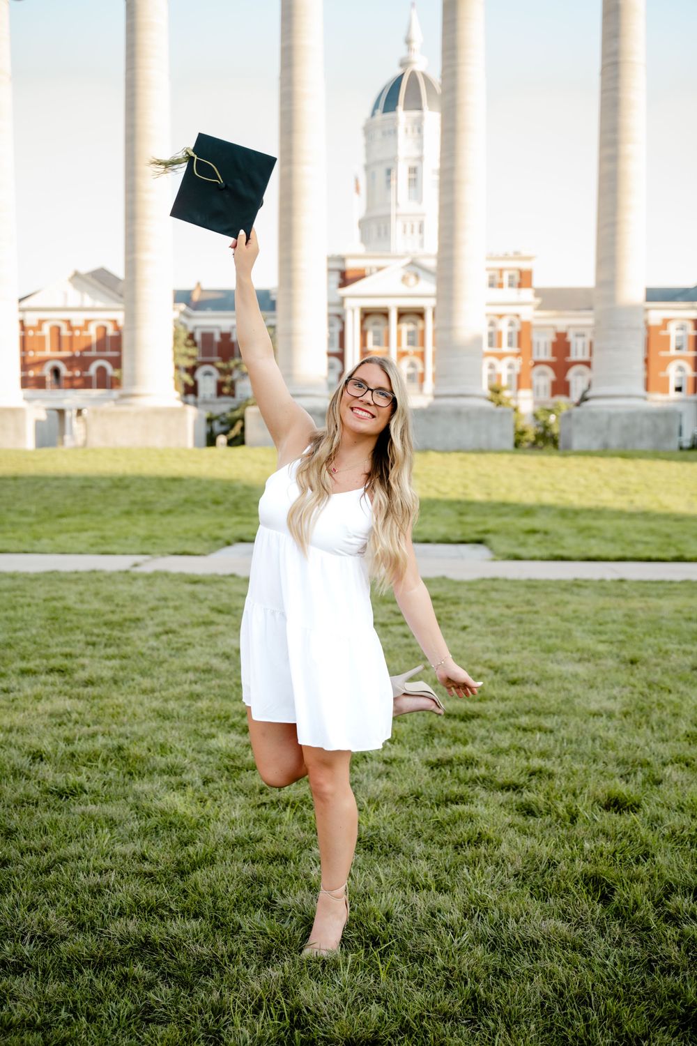 Graduate celebrates with cap toss on university quad with historic columns and dome in background.