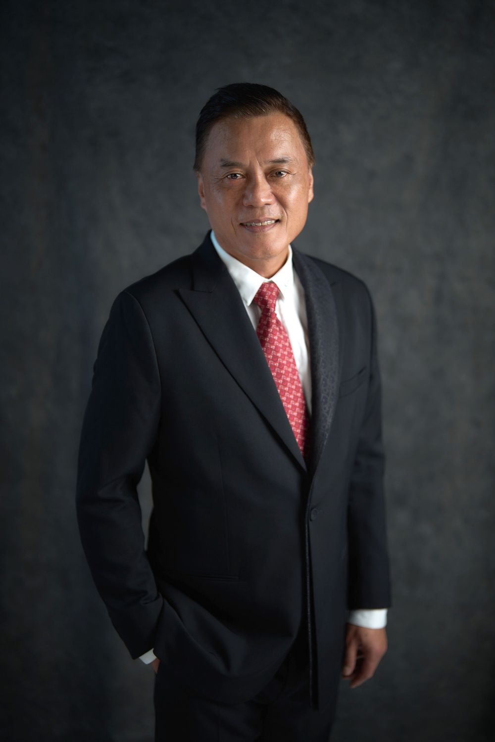 Professional business portraits of a man in a dark suit and red patterned tie against a dark backdrop.