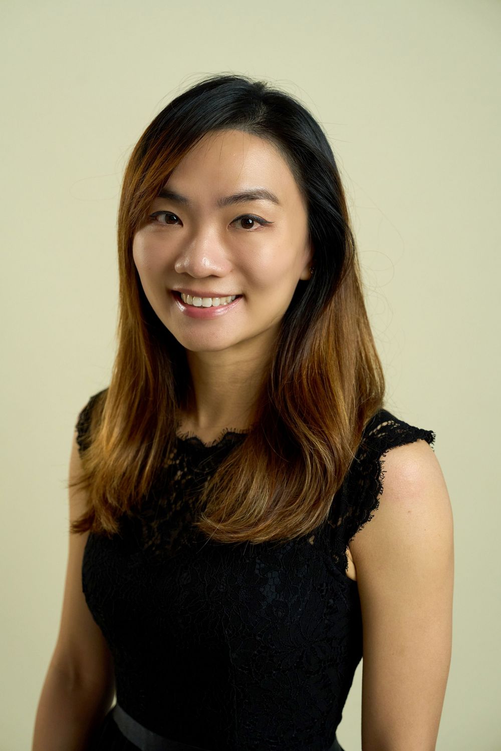 Woman in black sleeveless top smiling against light green background.