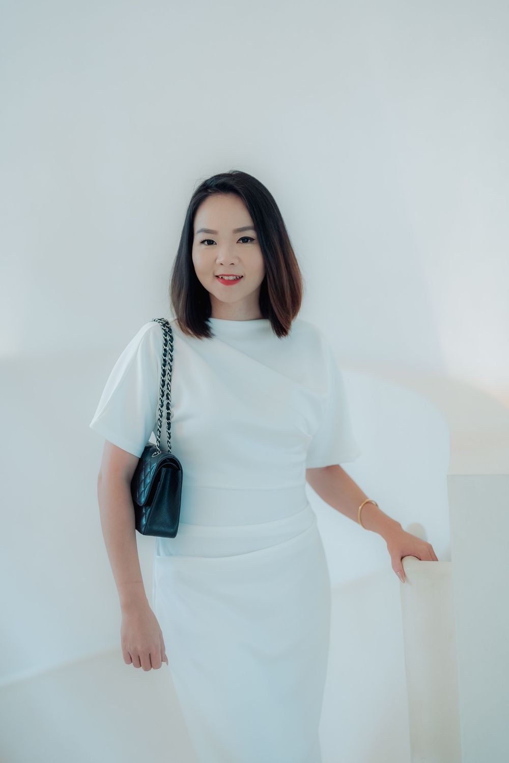 A person wearing a white dress and small black handbag poses against a light background in a minimalist fashion photo series.