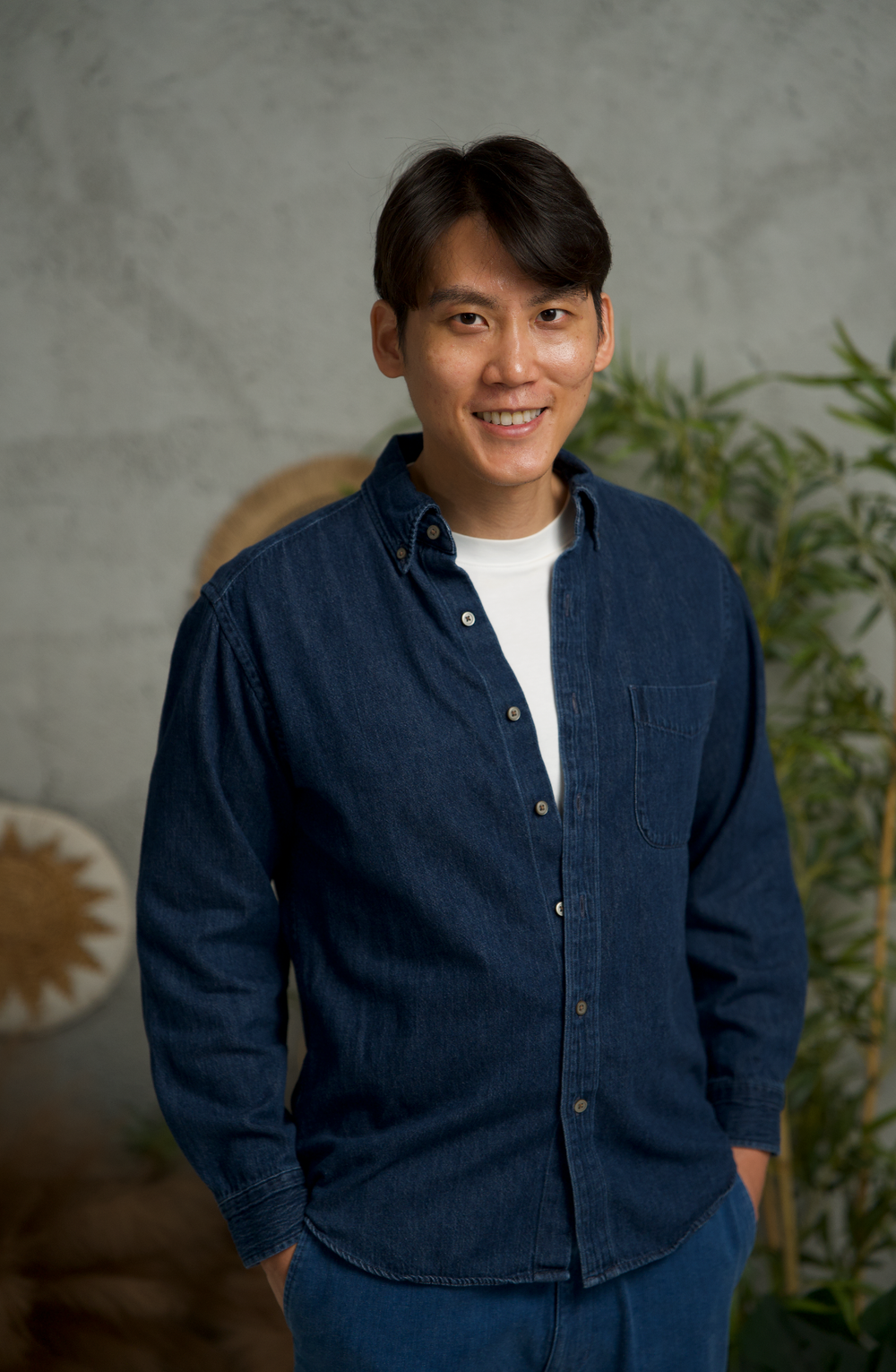 Portrait of person in navy button-down shirt against grey backdrop with decorative elements.