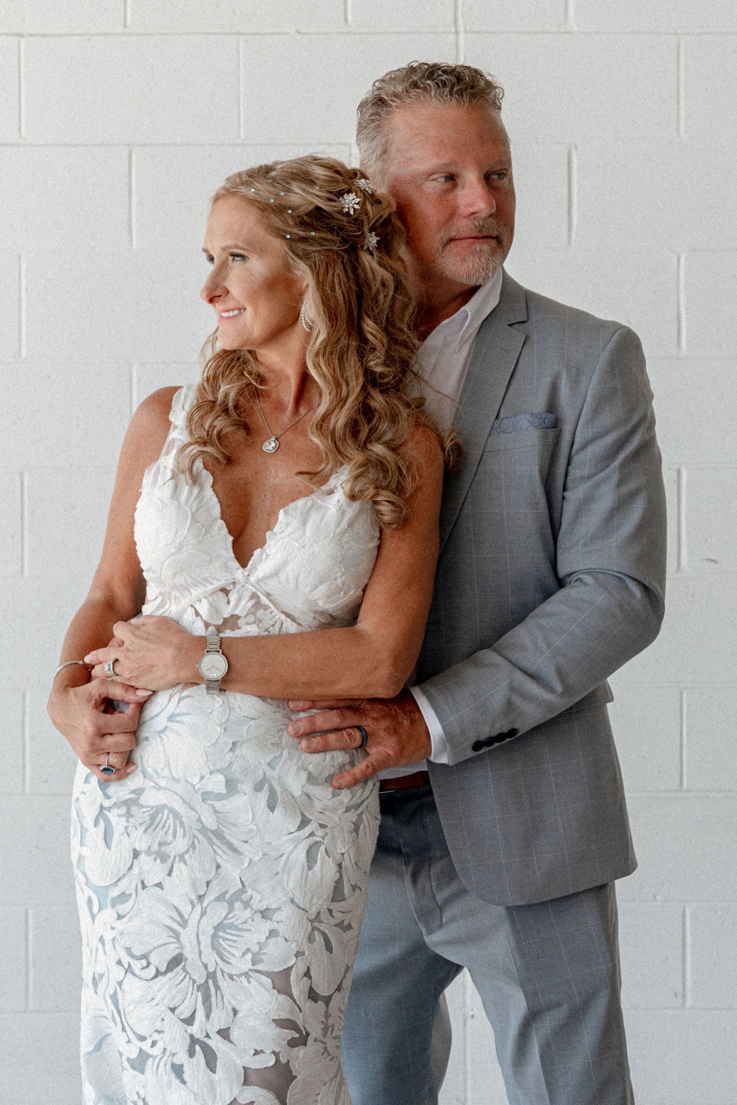 A couple in wedding attire embraces against a white brick wall in a romantic photoshoot sequence.
