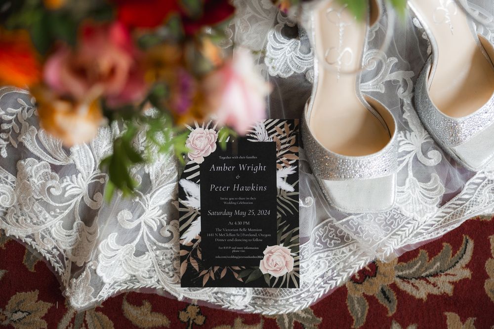 Wedding invitation and rings displayed with delicate lace details and floral elements on white background.