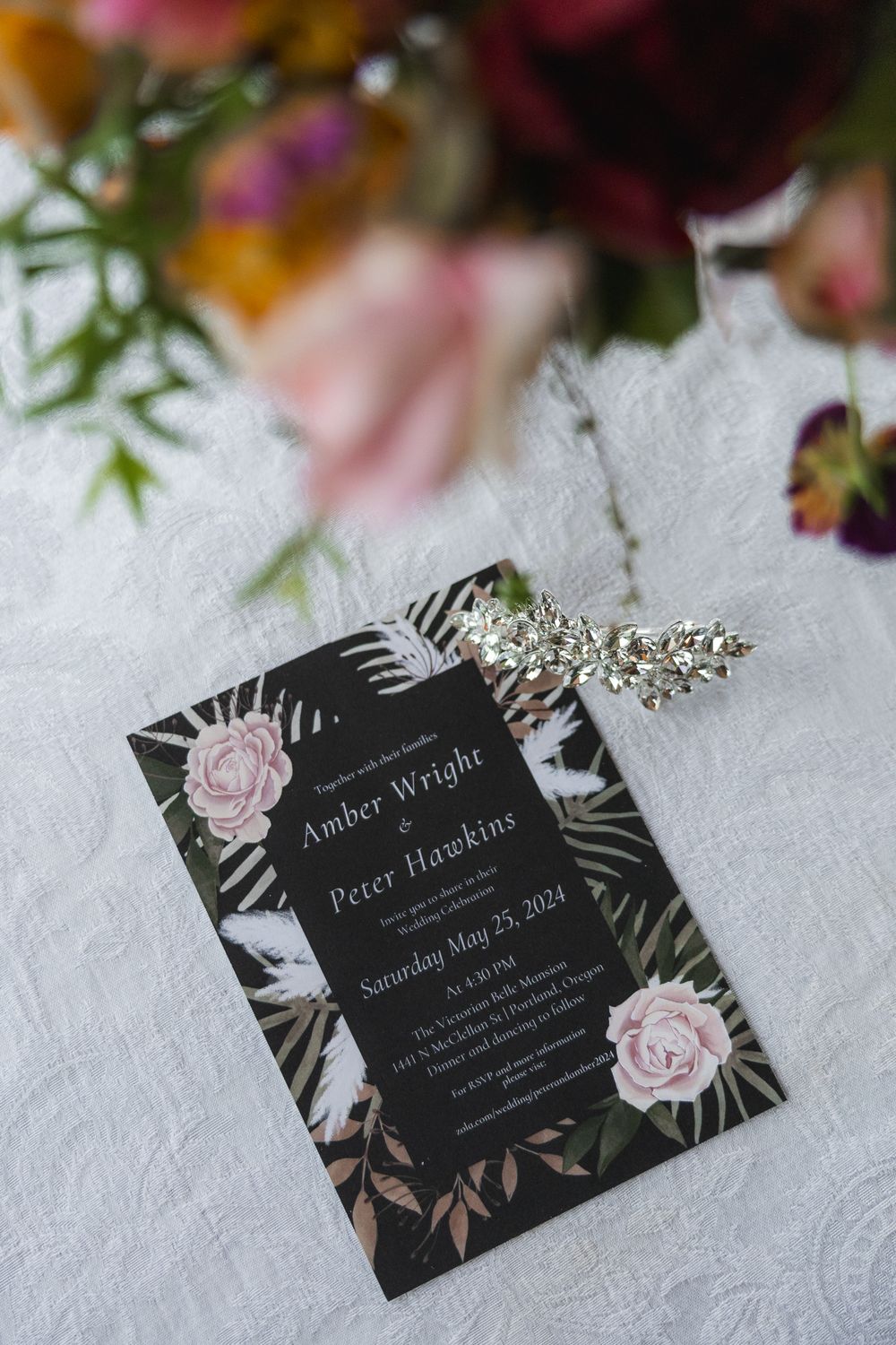 Black wedding invitation cards with floral designs and elegant typography lay on a textured white surface.
