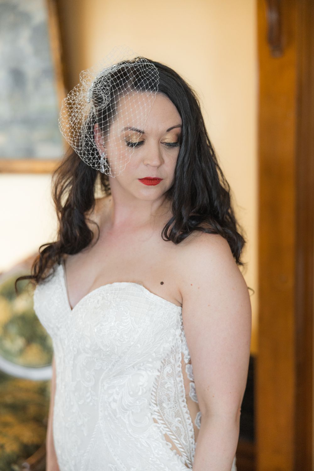 Close-up details of a bride wearing a delicate birdcage veil and white lace dress with red lipstick.