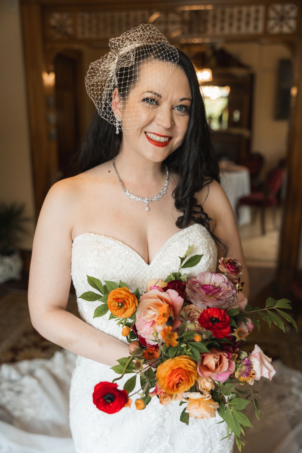 Close up of a bridal bouquet featuring vibrant orange, red and pink flowers with lush greenery against white fabric.