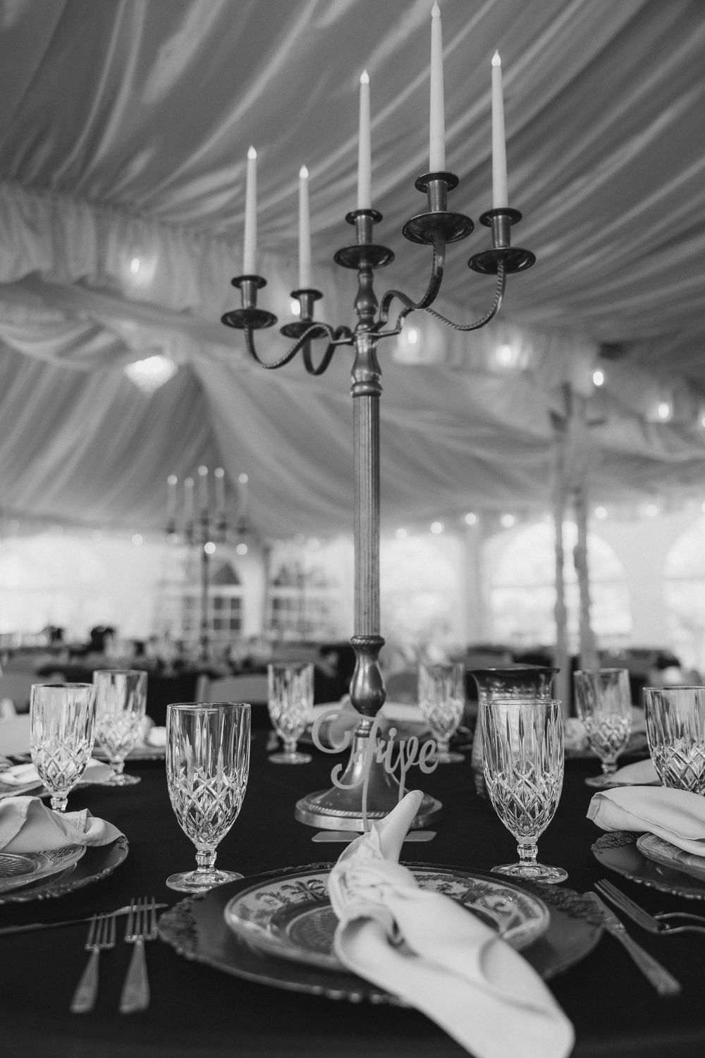 Elegant table setting with crystal glasses and candelabra under draped fabric ceiling at formal event.