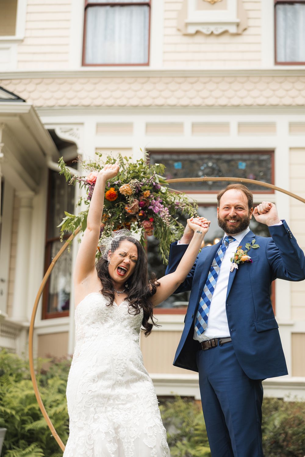 Joyful celebration moment in front of Victorian house with floral arch decoration.