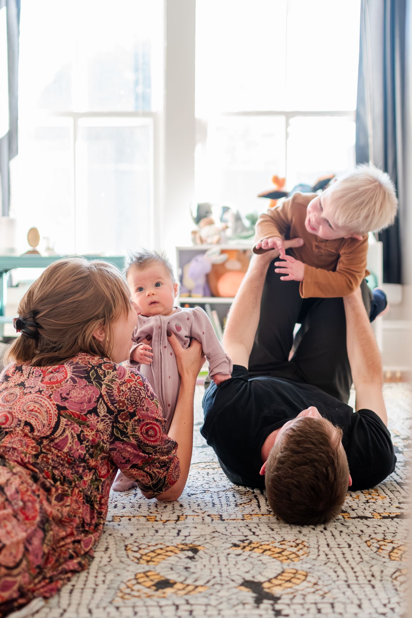 A sequence of four photos showing a baby and adult lying on a patterned carpet, rolling and playing together.
