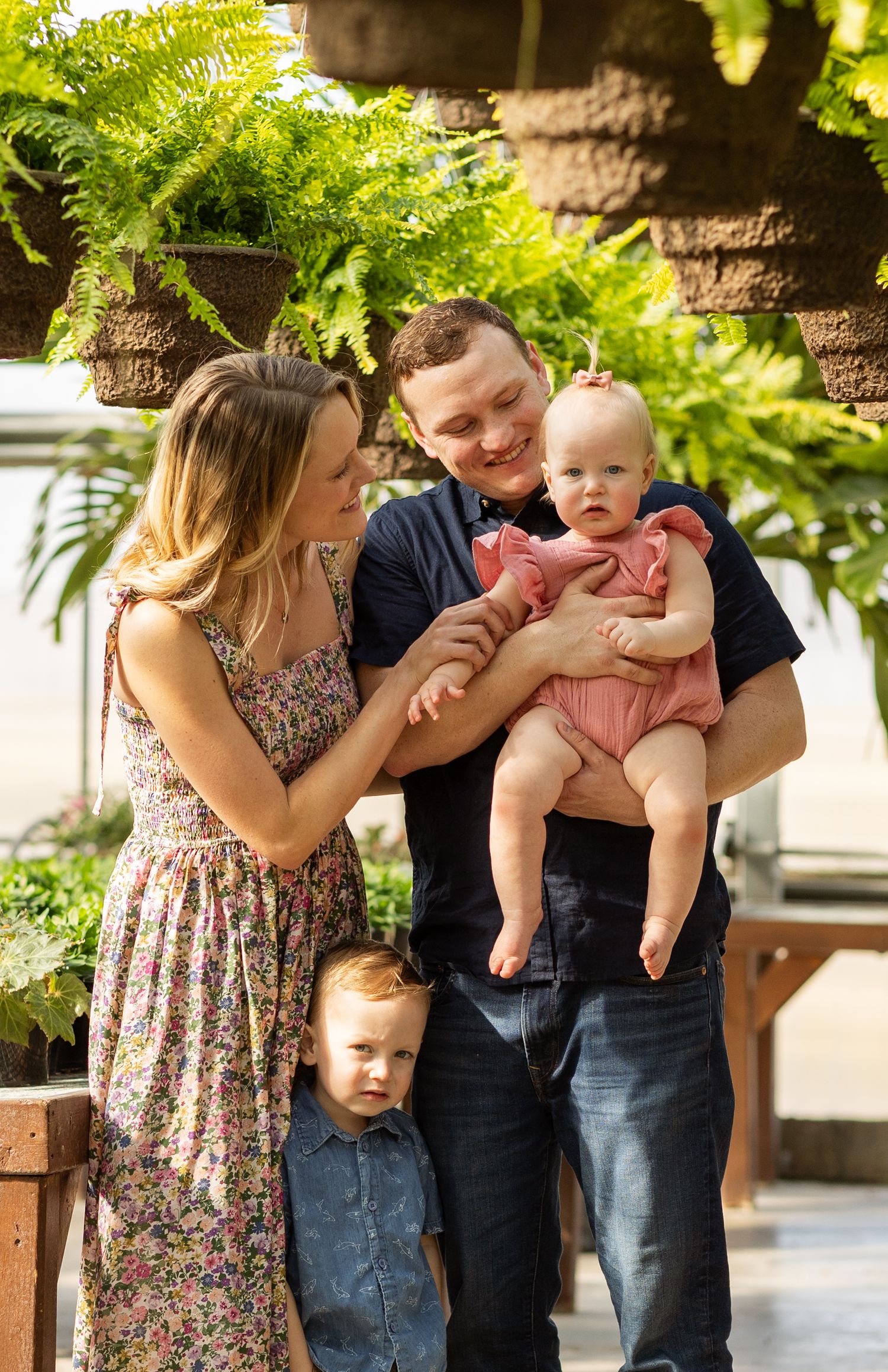 Candid family moment in a greenhouse with lush ferns and natural lighting.