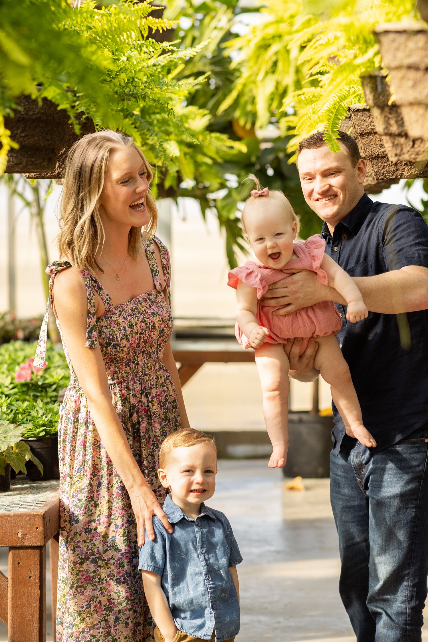 Joyful family laughing together in a greenhouse setting with hanging ferns.