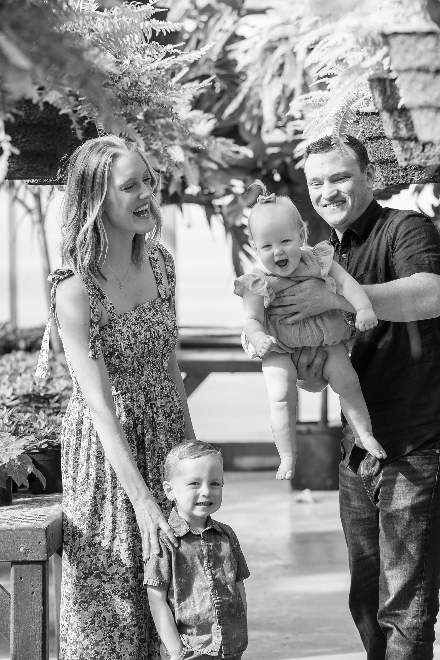 A joyful black and white family portrait under hanging plants in a greenhouse setting.