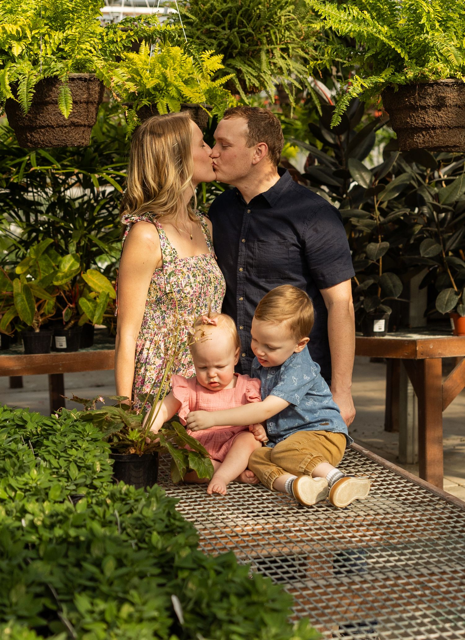 An intimate family portrait surrounded by lush greenhouse plants and hanging ferns.