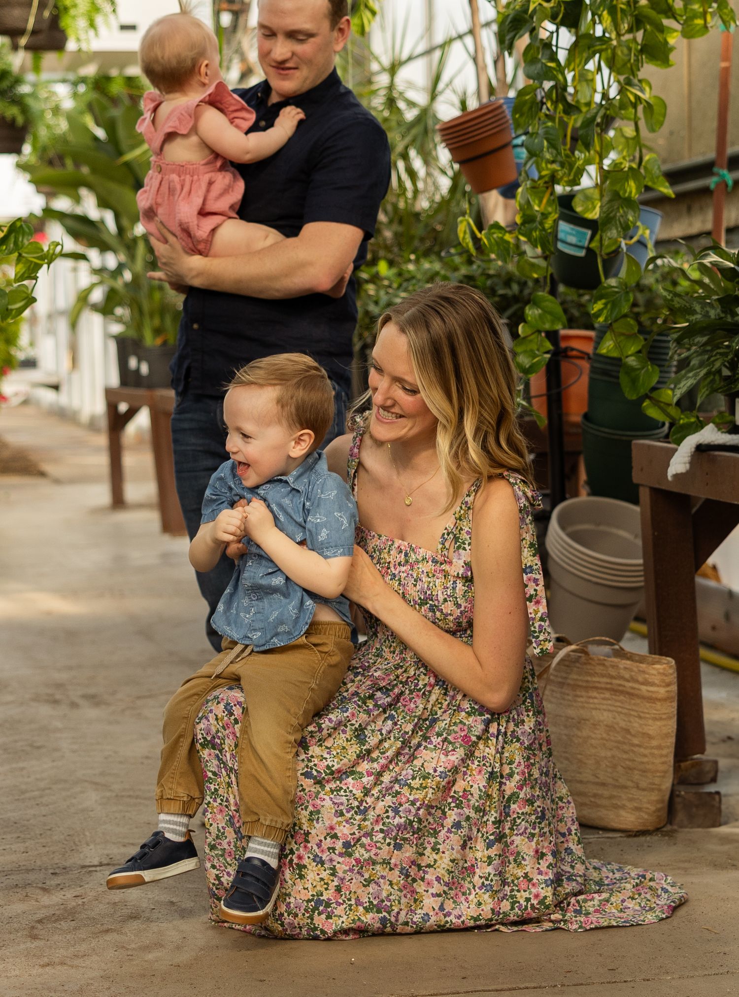 Family sharing tender moments among greenhouse plants and wooden displays.