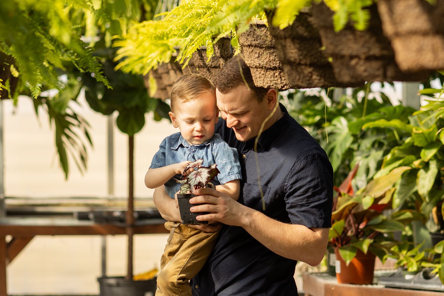 A candid moment looking at a camera together in a greenhouse surrounded by lush ferns and hanging plants.