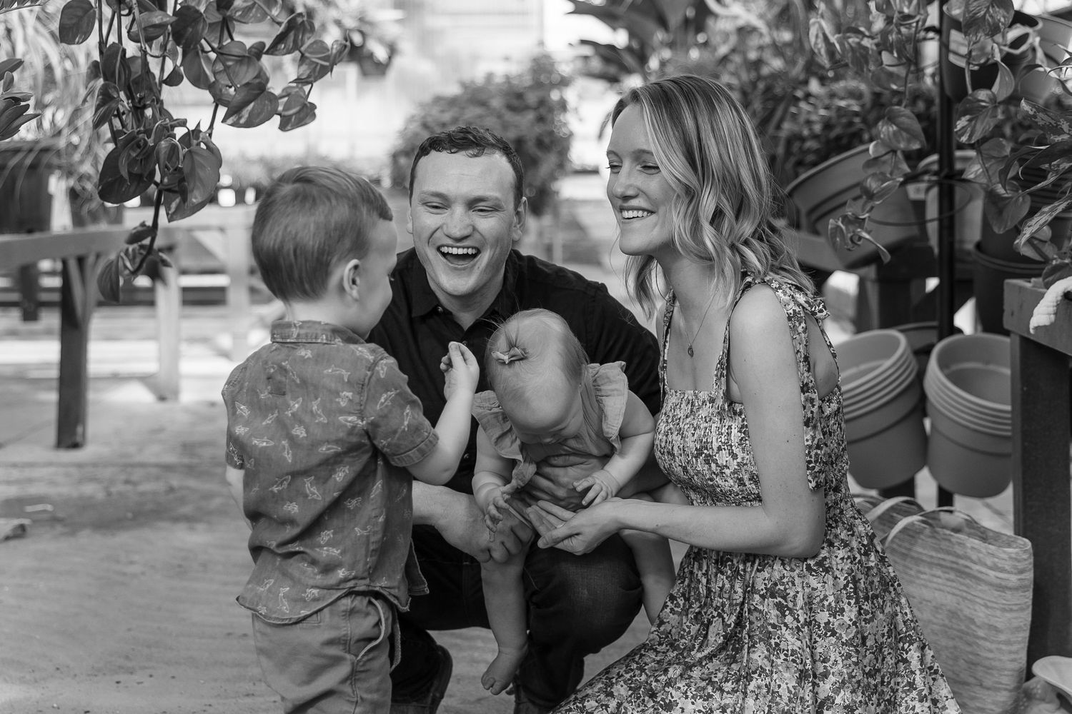 Black and white photo of family sharing joyful moments in greenhouse setting.