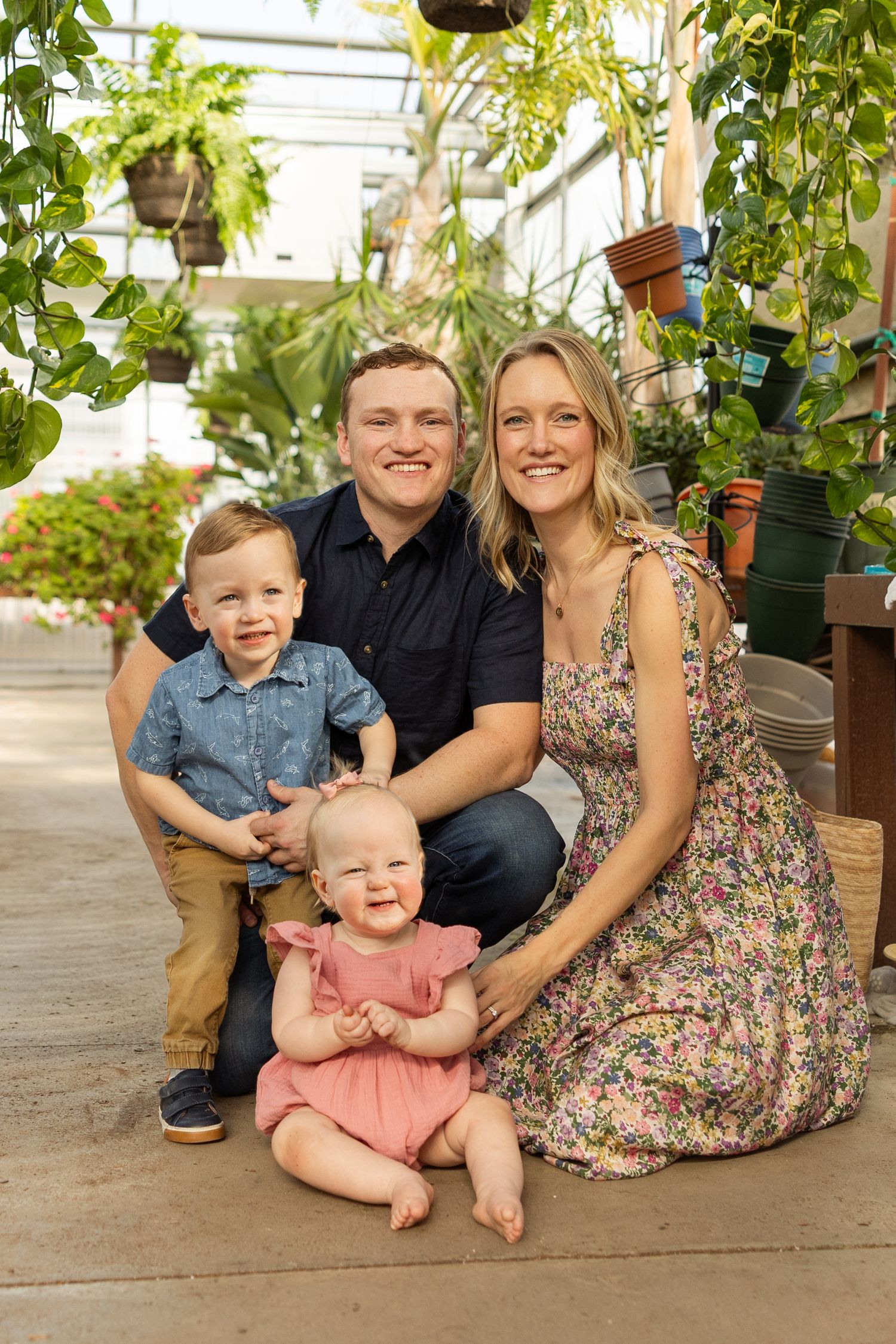 Family poses together in a greenhouse with lush greenery and natural lighting.