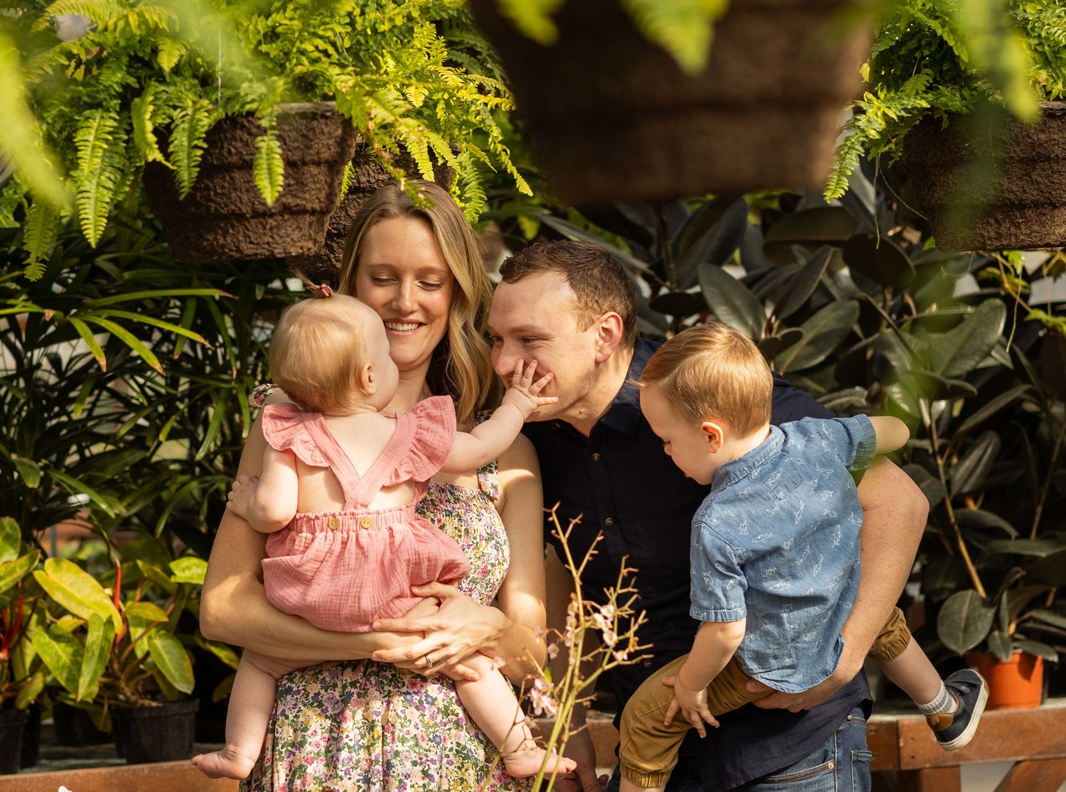 Candid family portrait under hanging ferns in a greenhouse setting.