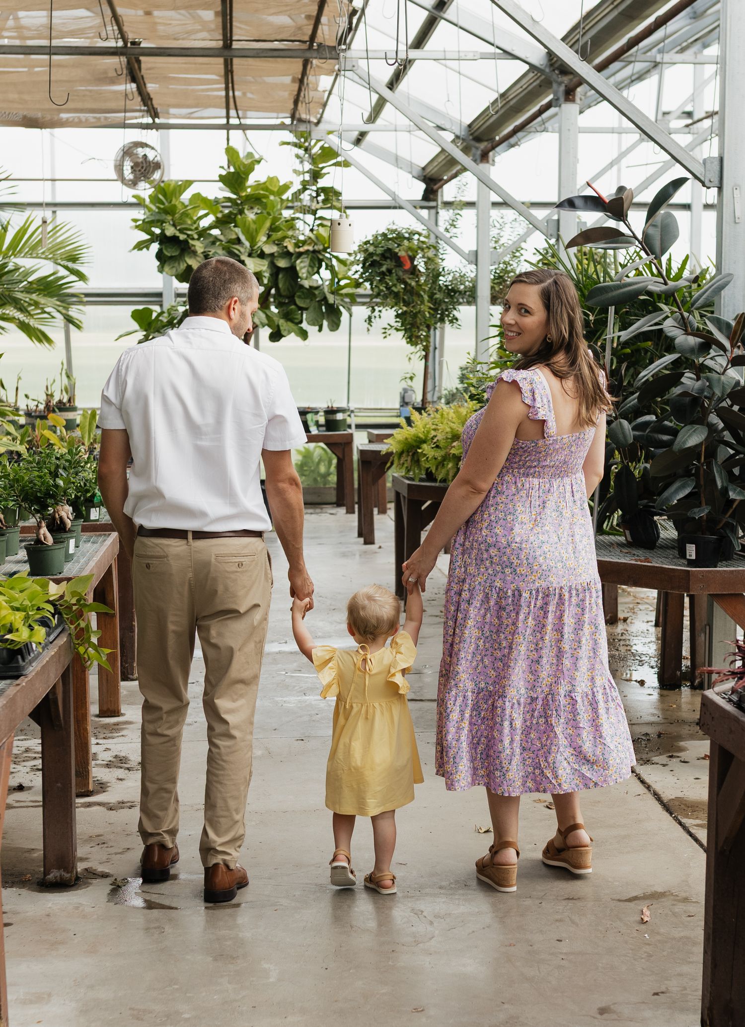 Family exploring together in a bright greenhouse with potted plants and wooden benches.