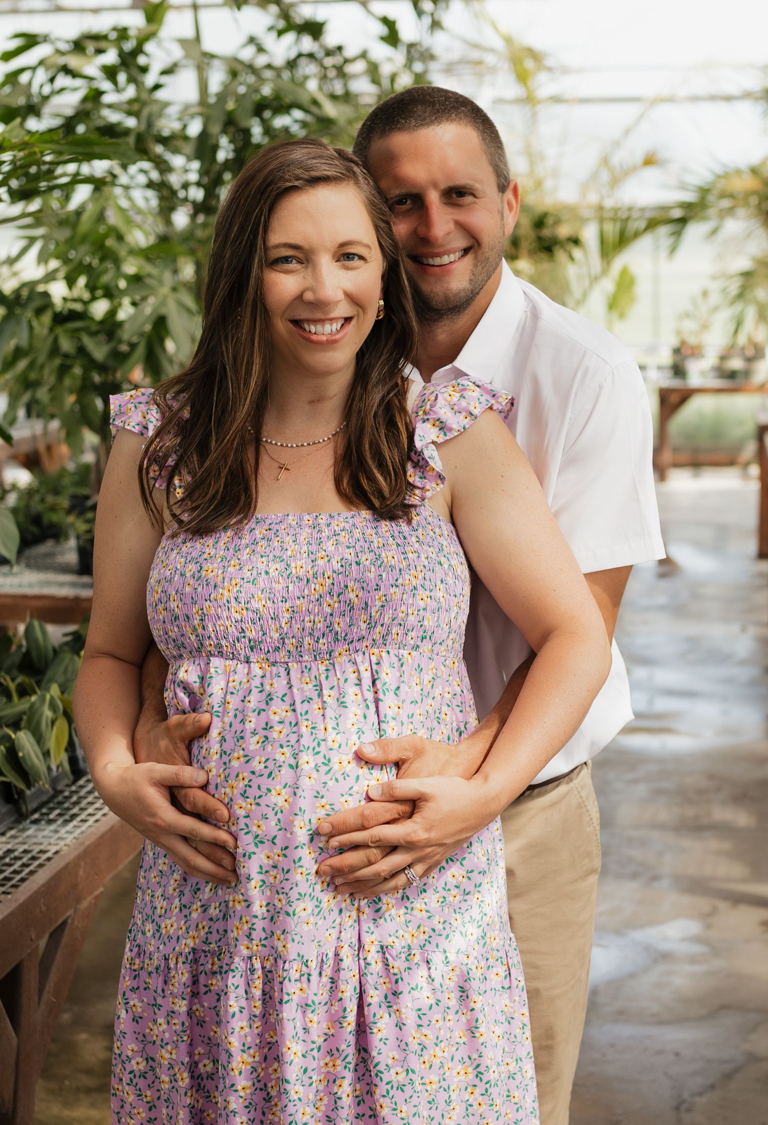 Romantic greenhouse maternity session with couple in white and floral attire.