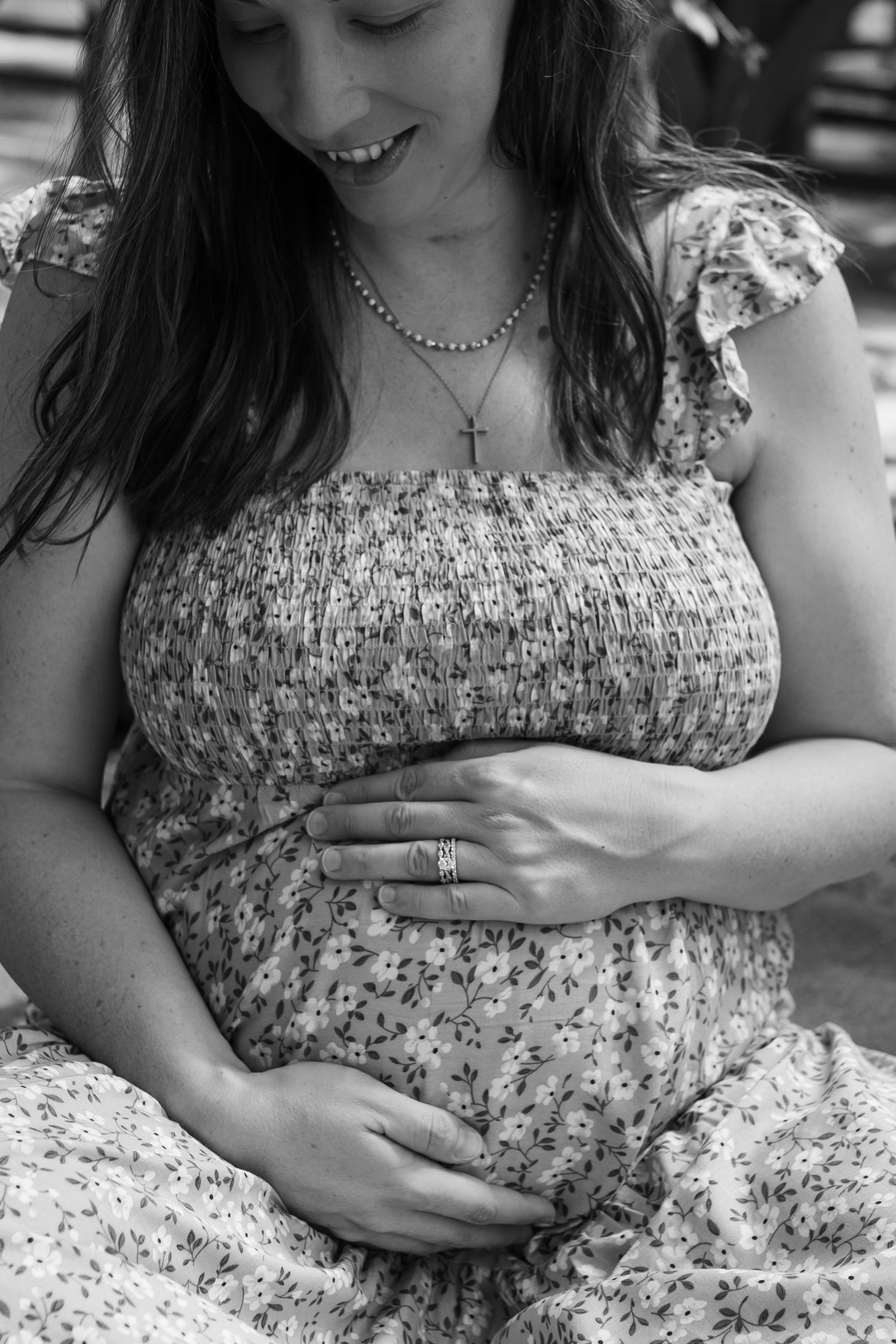 Black and white close-up of a floral dress and hands cradling a pregnant belly.
