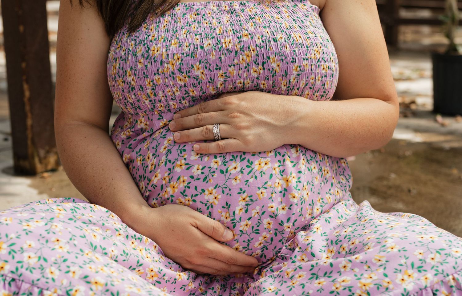 Close-up detail of hands resting on a floral patterned maternity dress.