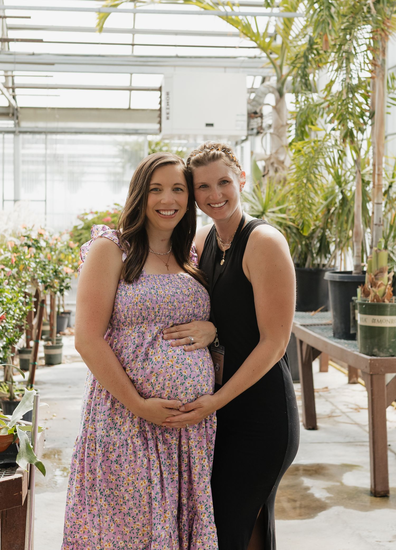 Two people embrace in a greenhouse setting with potted plants and natural light.